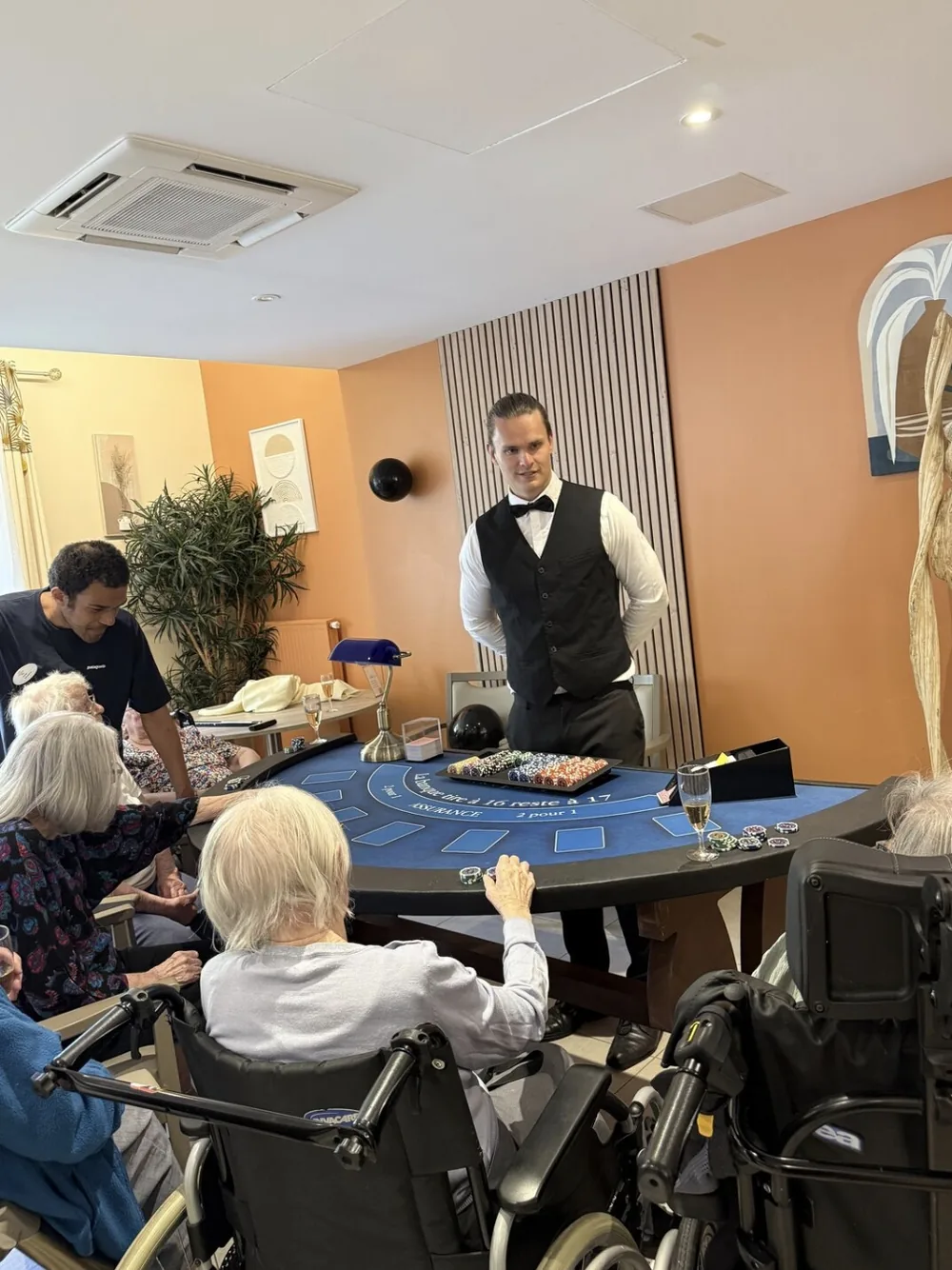 Table de blackjack animée par un croupier, entourée de résidents dont plusieurs installés en fauteuil roulant