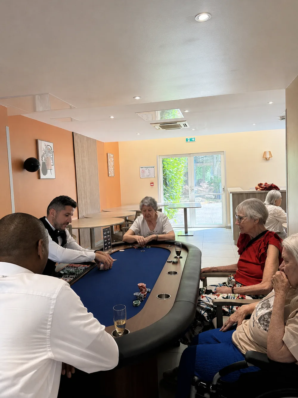 Croupier distribuant les cartes sur la table de poker devant des résidents de l'EHPAD