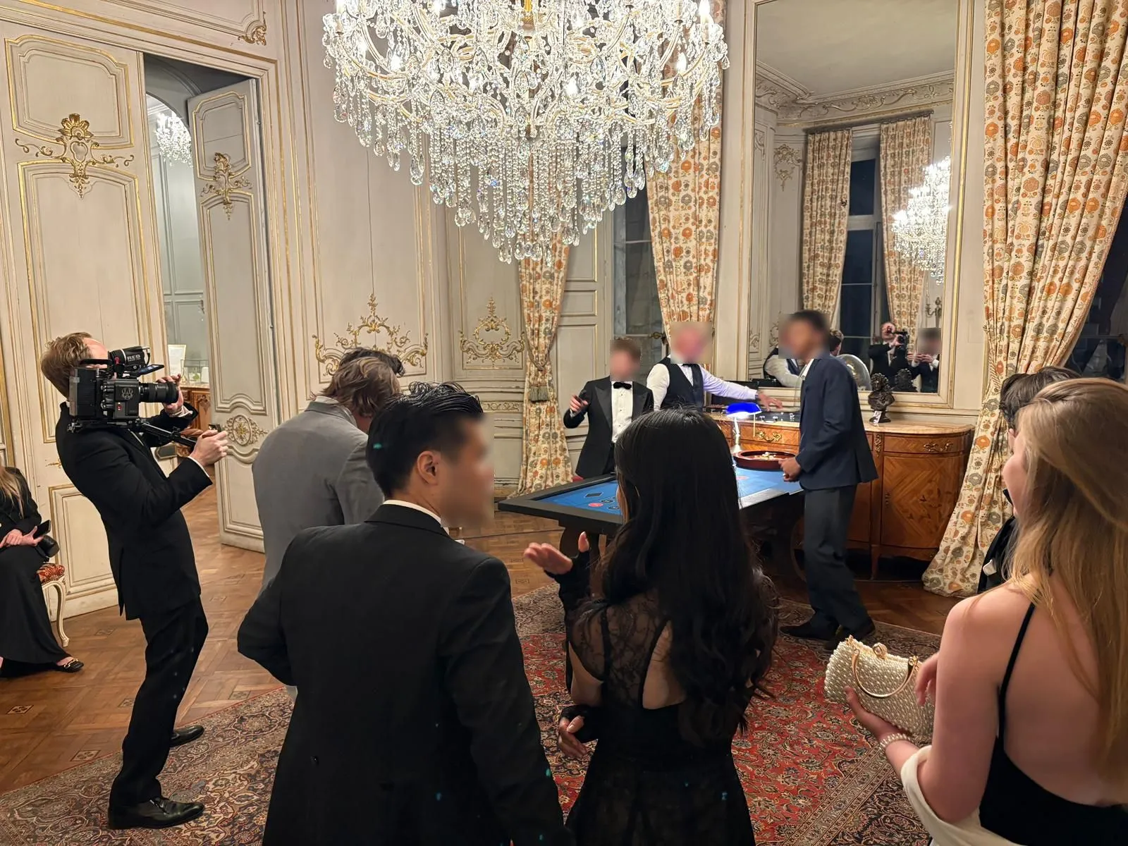 Invités en tenue de soirée autour des tables de casino sous le grand lustre du château